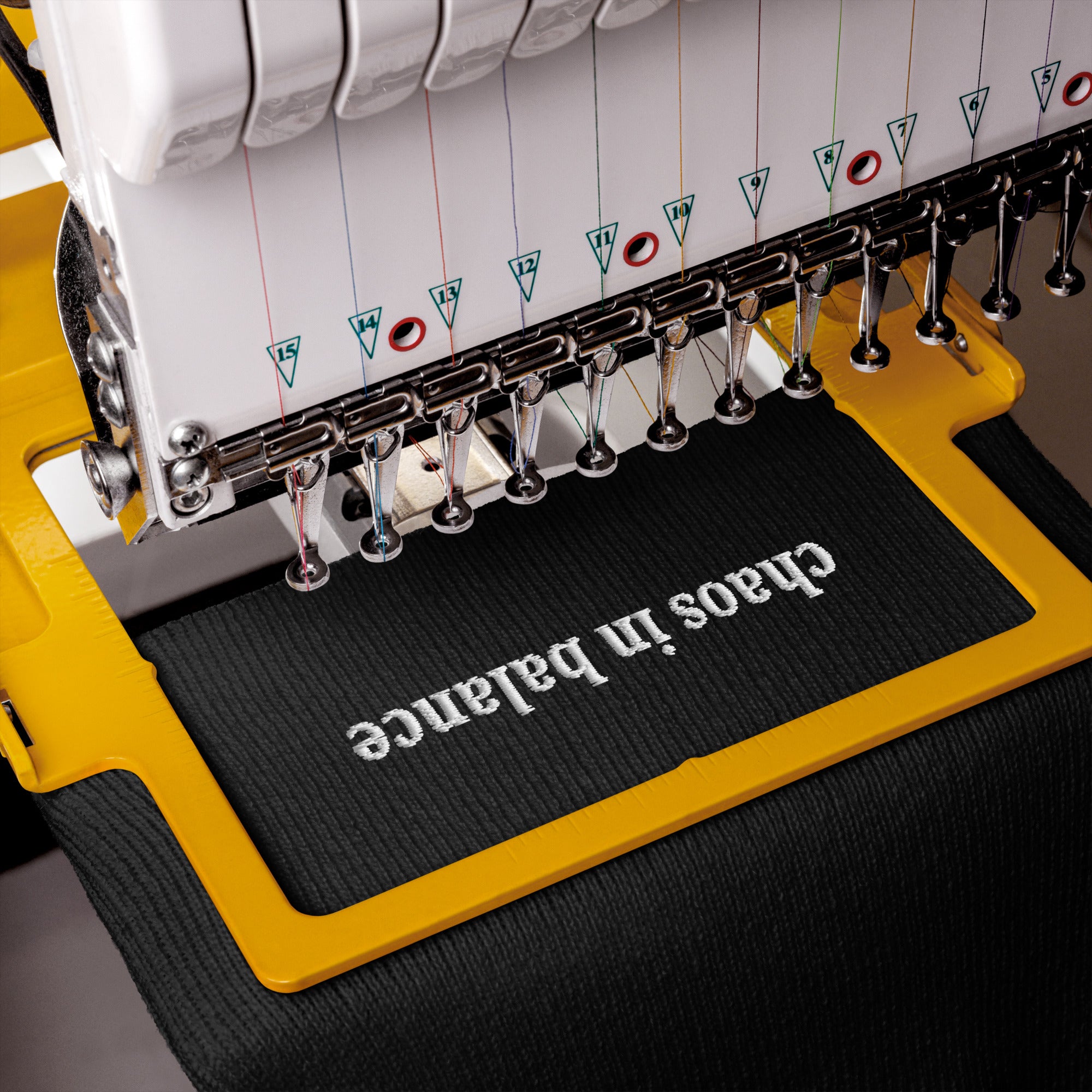 Embroidery machine with 'chaos in balance' text on a black beanie