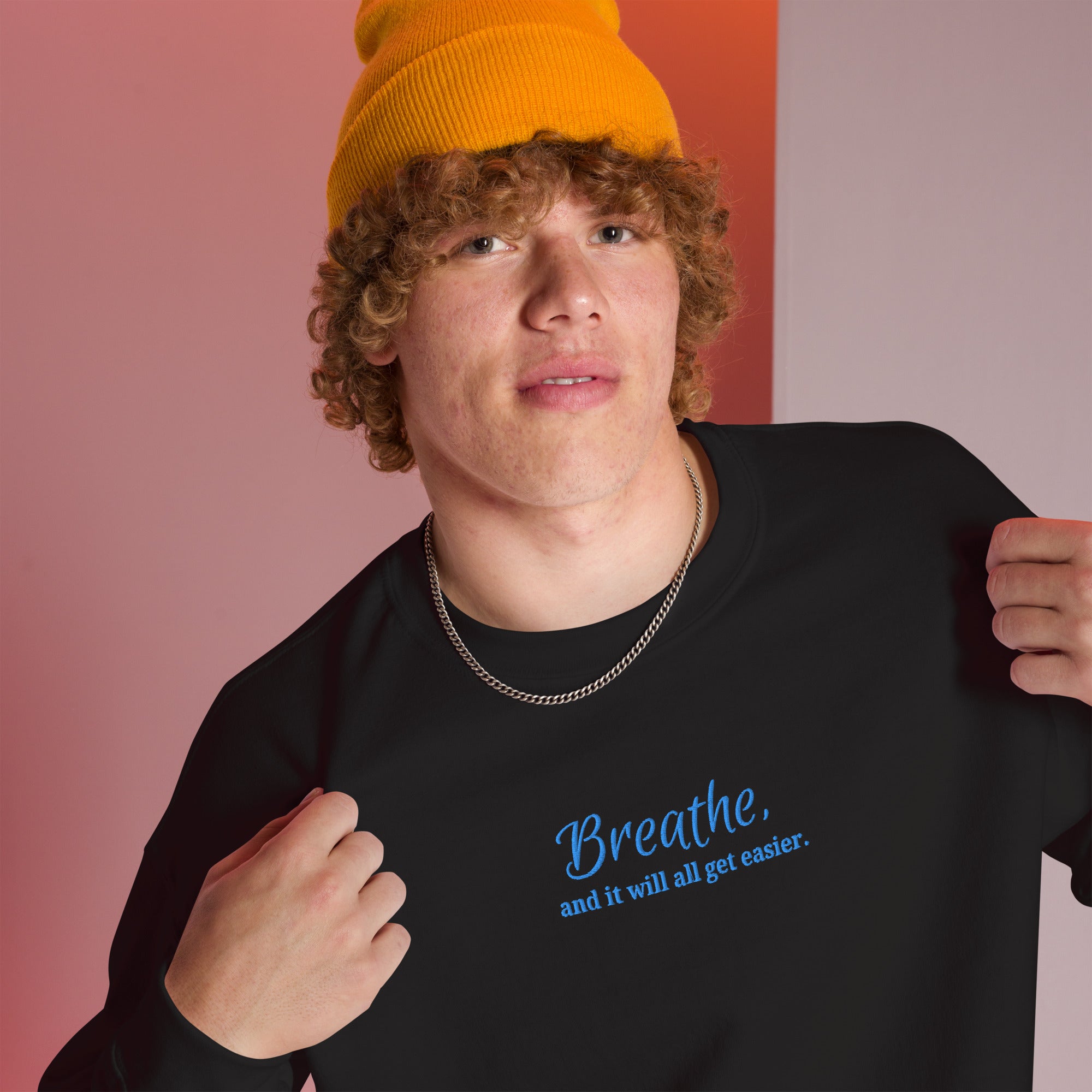 Person wearing a black sweatshirt with embroidered 'Breathe. and it will all get easier, quote