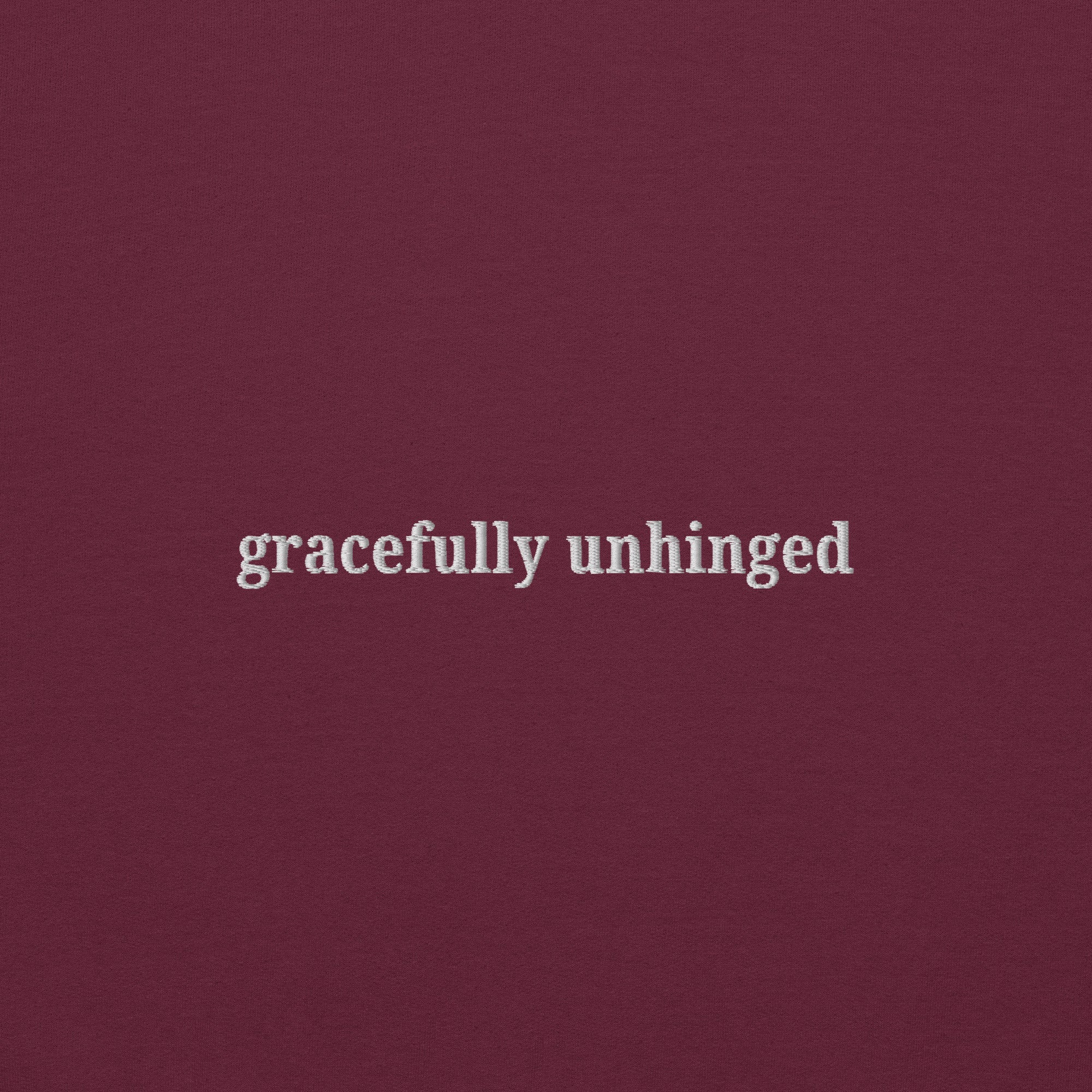 white thread embroidery reading Gracefully Unhinged on unisex maroon Gildan sweatshirt