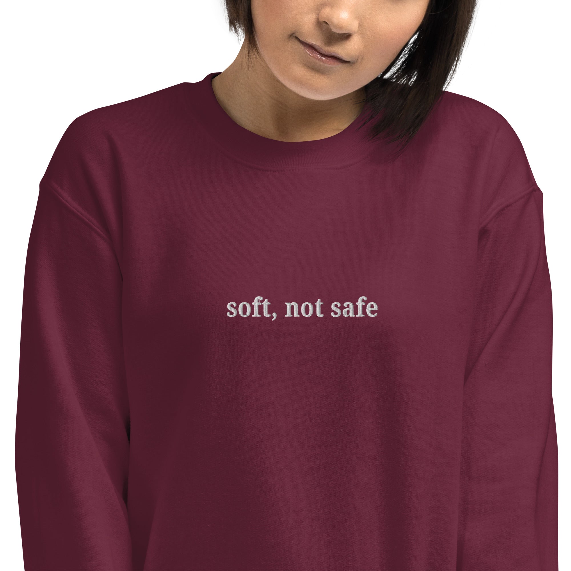 Person wearing a maroon sweatshirt with 'soft, not safe' text embroidered  on maroon sweatshirt