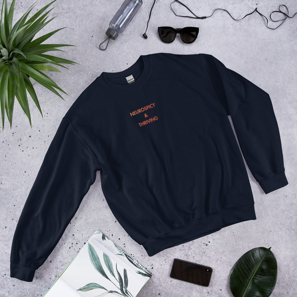 flat lay of Neurospicy and Thriving sweatshirt showing centre-chest gradient embroidery on navy sweatshirt