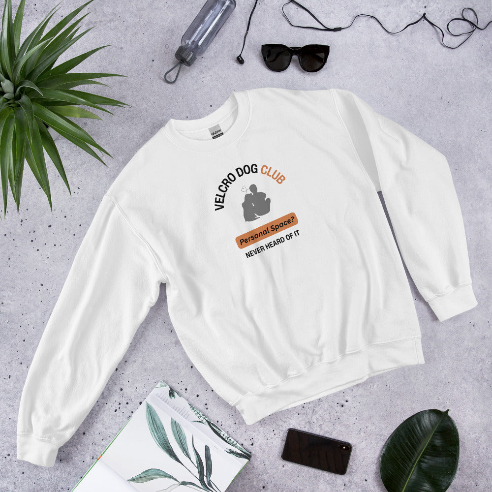 White sweatshirt with 'Velcro Dog Club' design on a gray surface with plants and accessories.