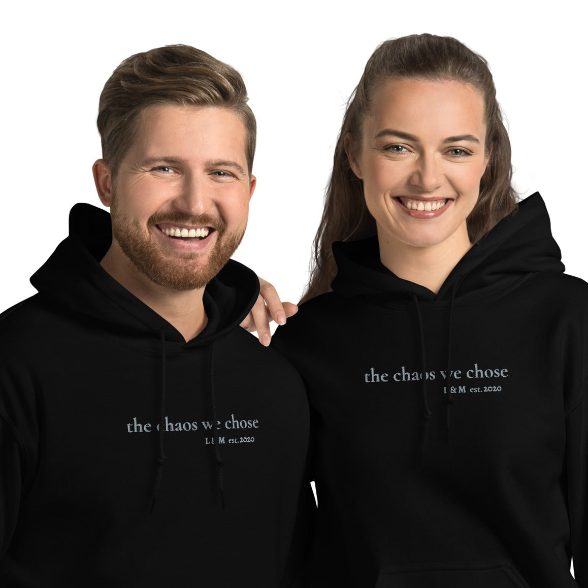 Couple wearing embroidered ‘The Chaos We Chose’ hoodie in grey thread — personalised with initials and year, unisex fit, available in black, maroon, dark chocolate, and sand