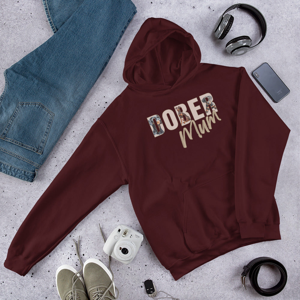 Maroon hoodie with 'DOBER MUM' text, surrounded by jeans, shoes, camera, and phone on a gray surface.