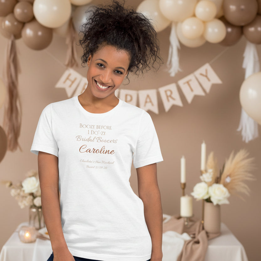 White personalised bridal party t-shirt featuring party member name and “Boozy Before I Do’zy” text, styled for a hen weekend.