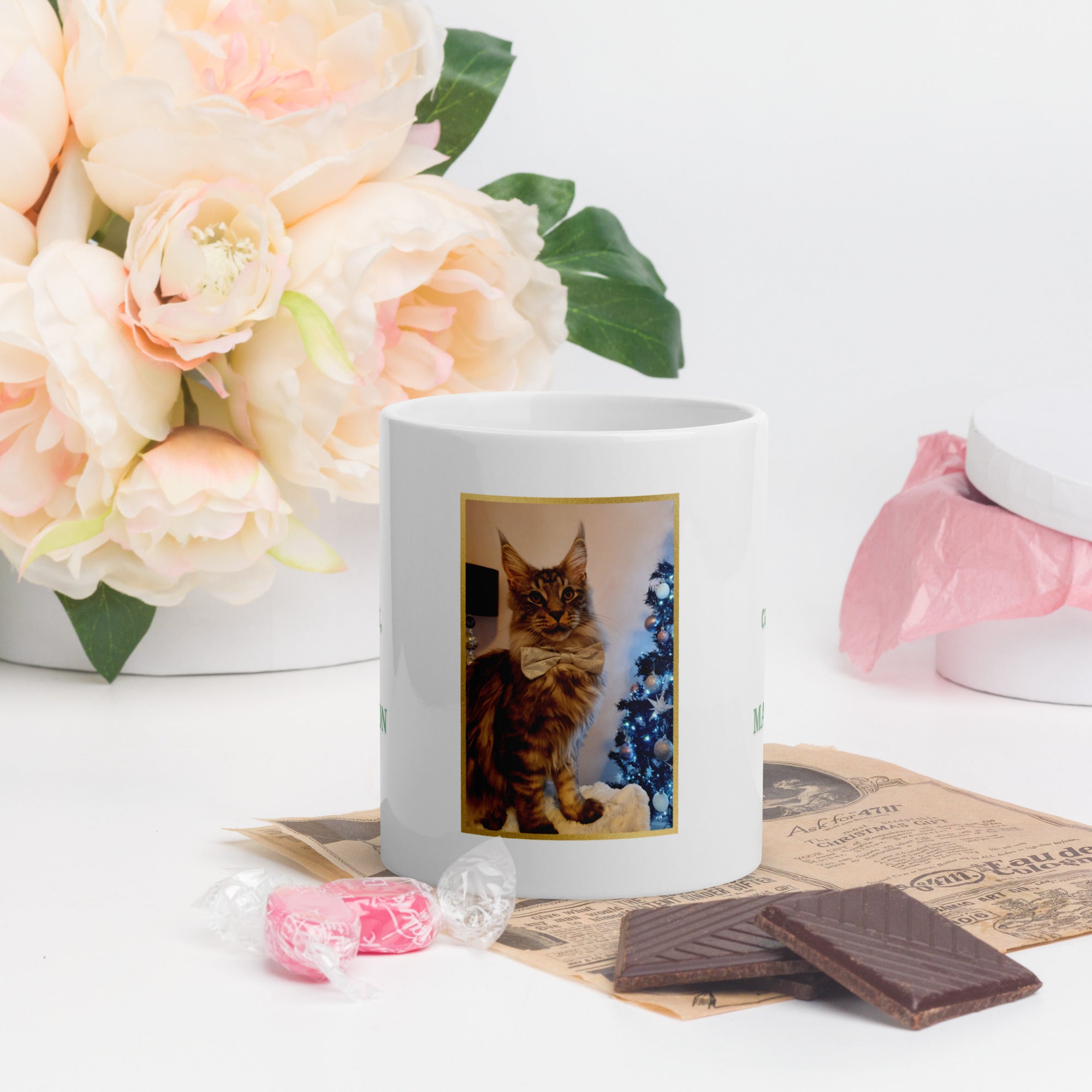 White mug with a cat photo on a table with flowers and chocolates