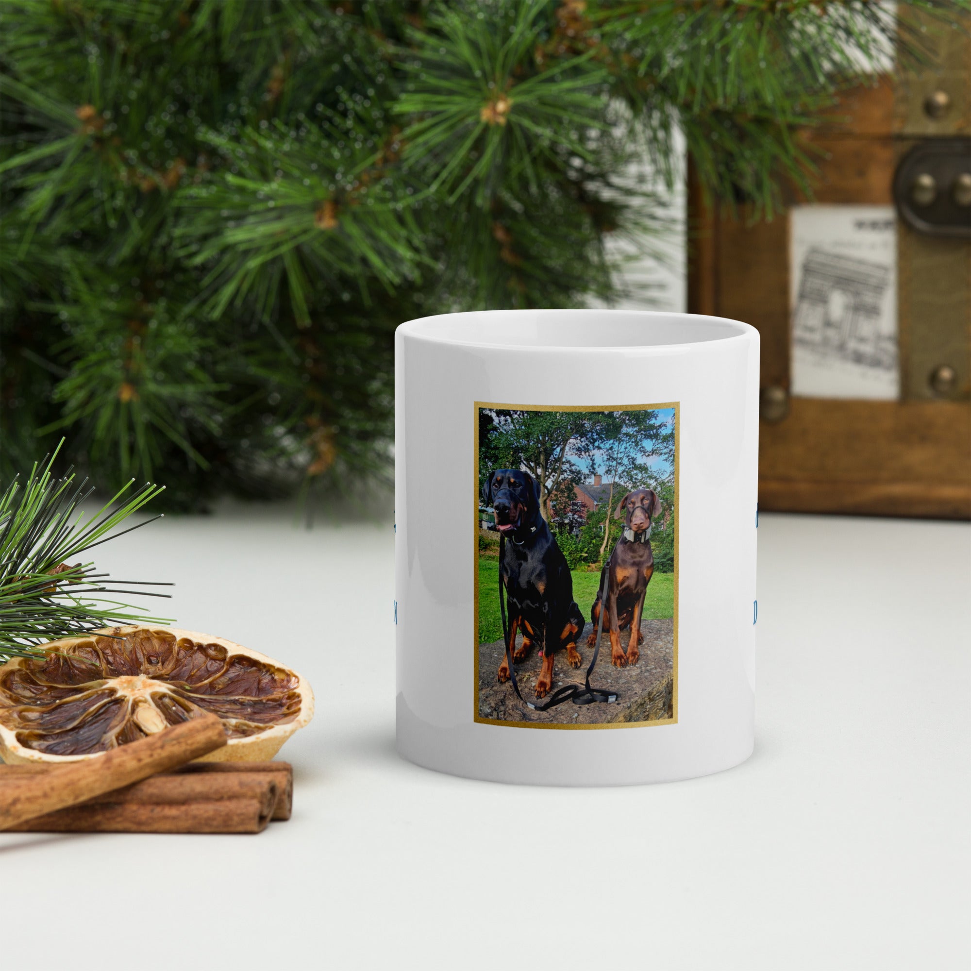 White mug with a picture of two dogs on a table with Christmas decorations.