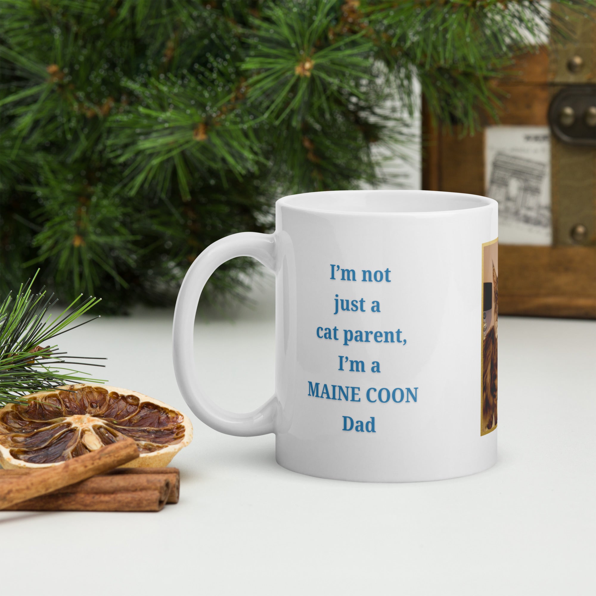 White mug with text about a Maine Coon cat parent on a table with decorative elements.