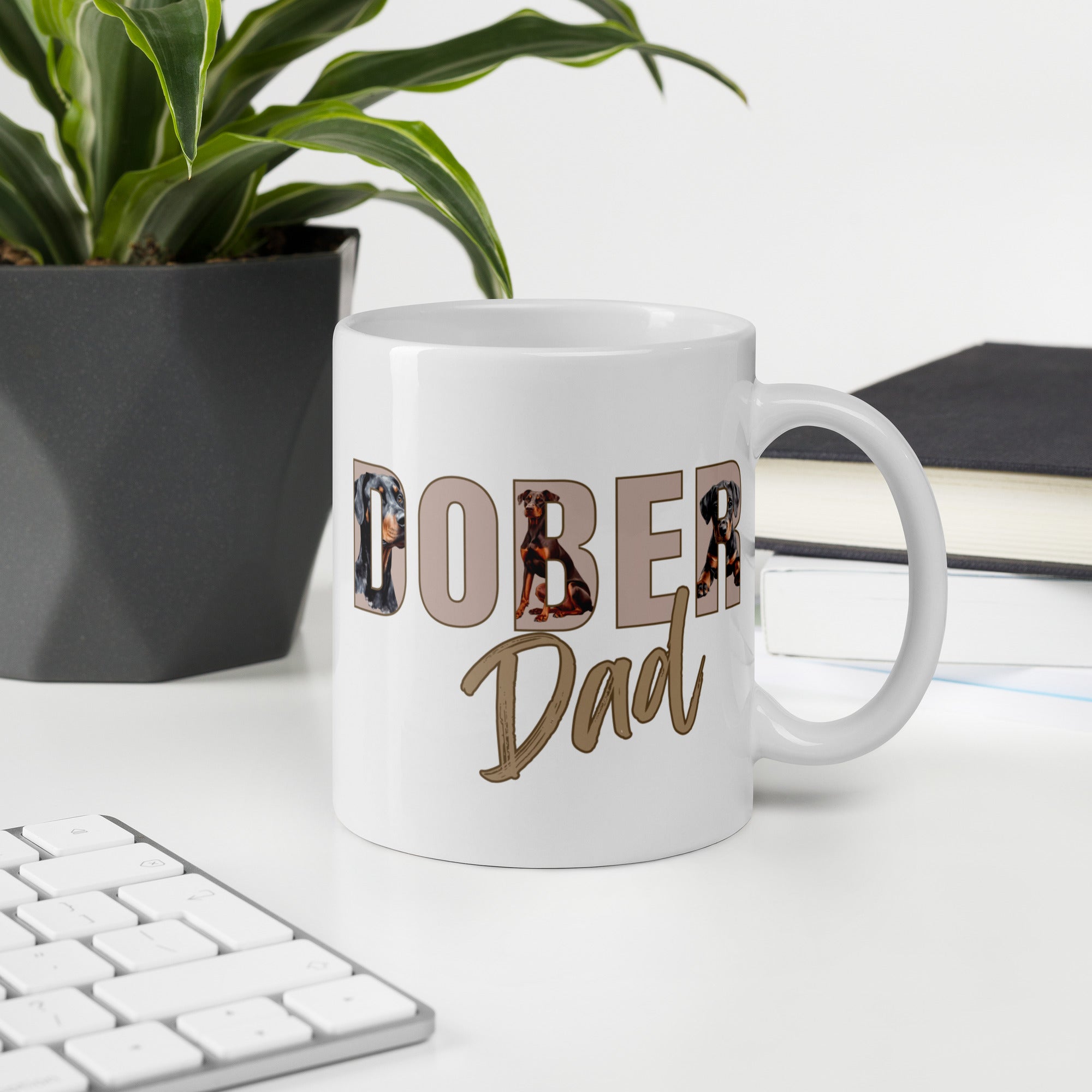 White mug with 'Dober Dad' text on a desk with a plant and books in the background