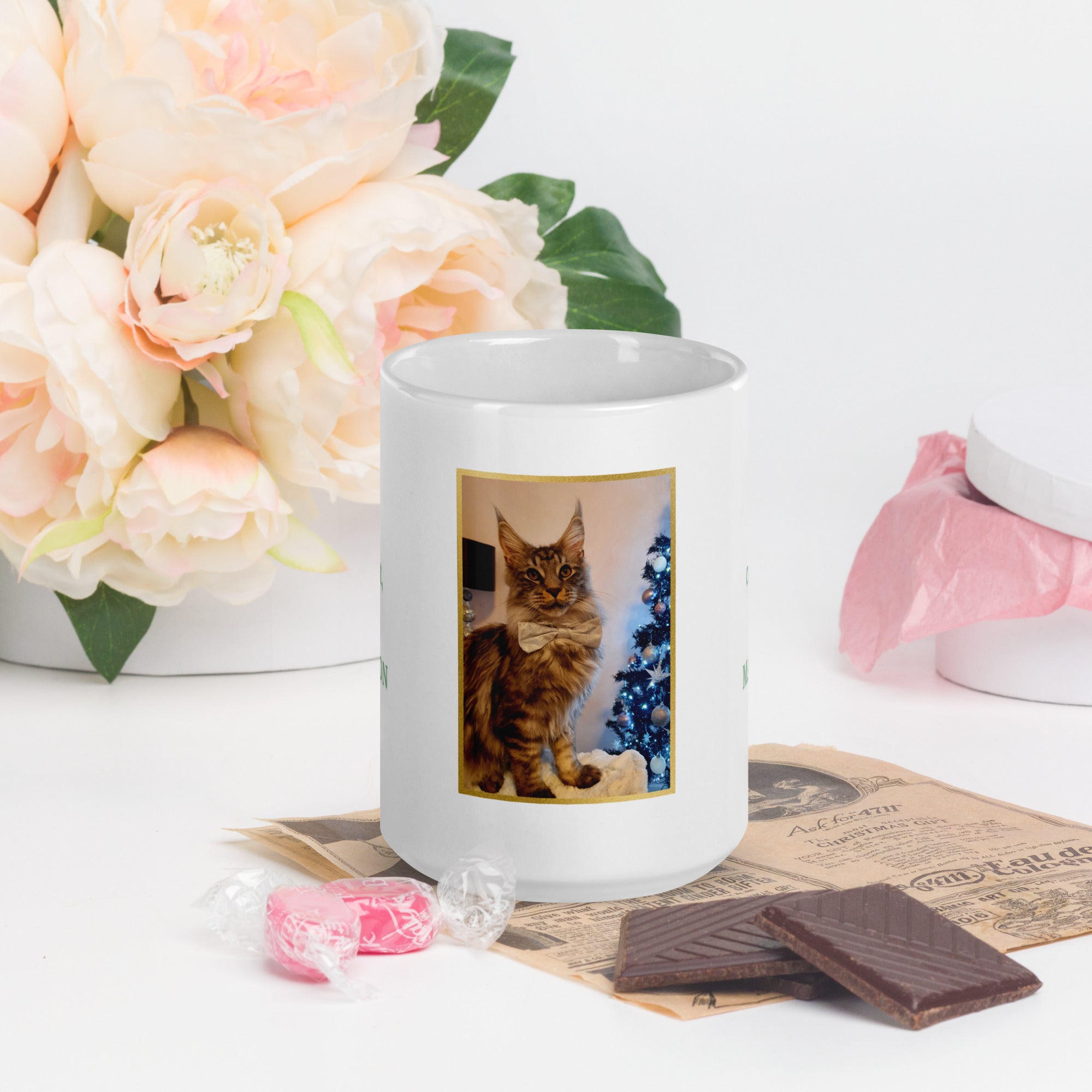 White mug with a cat photo on a table with flowers and chocolates