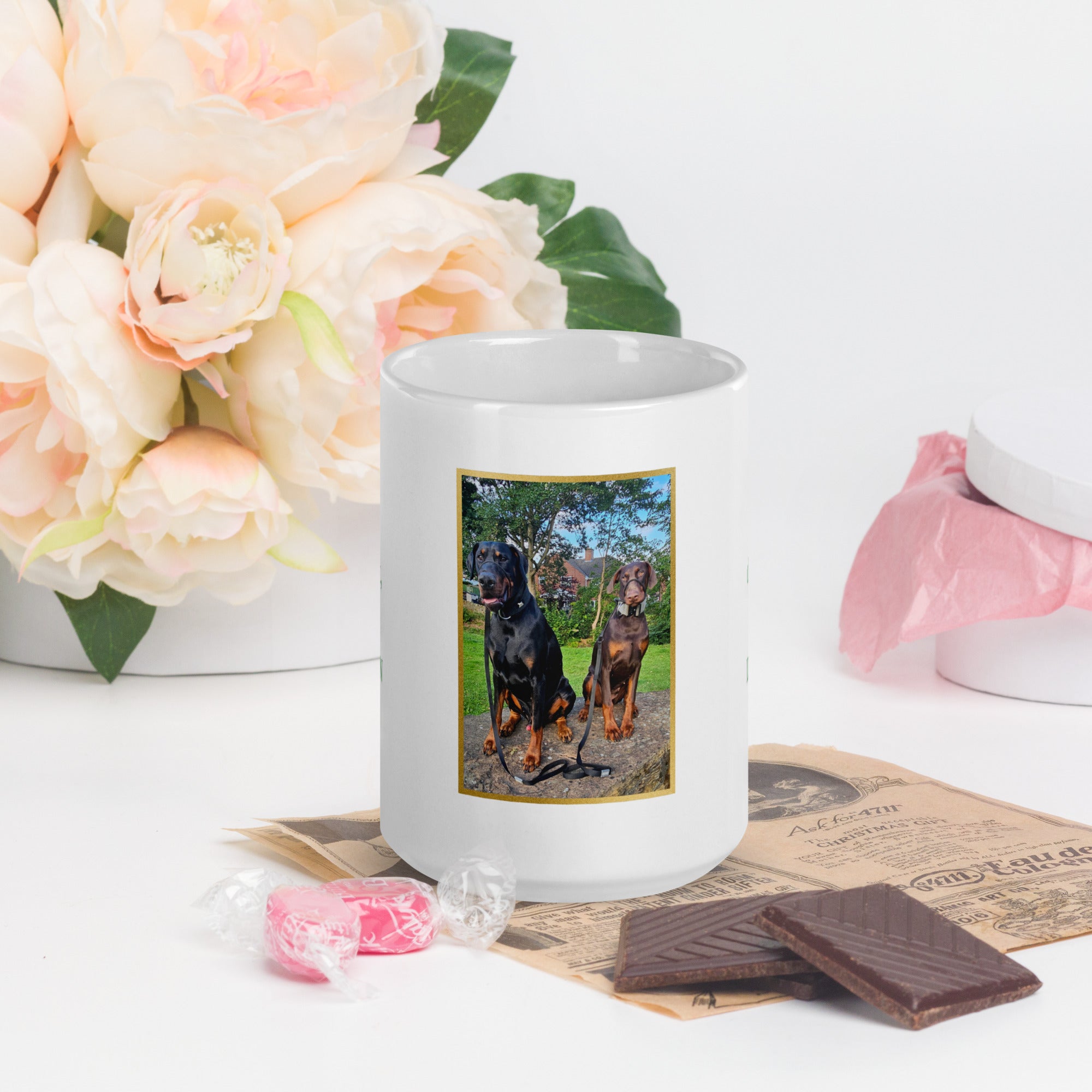White mug with a picture of two dogs on a table with flowers and chocolate.