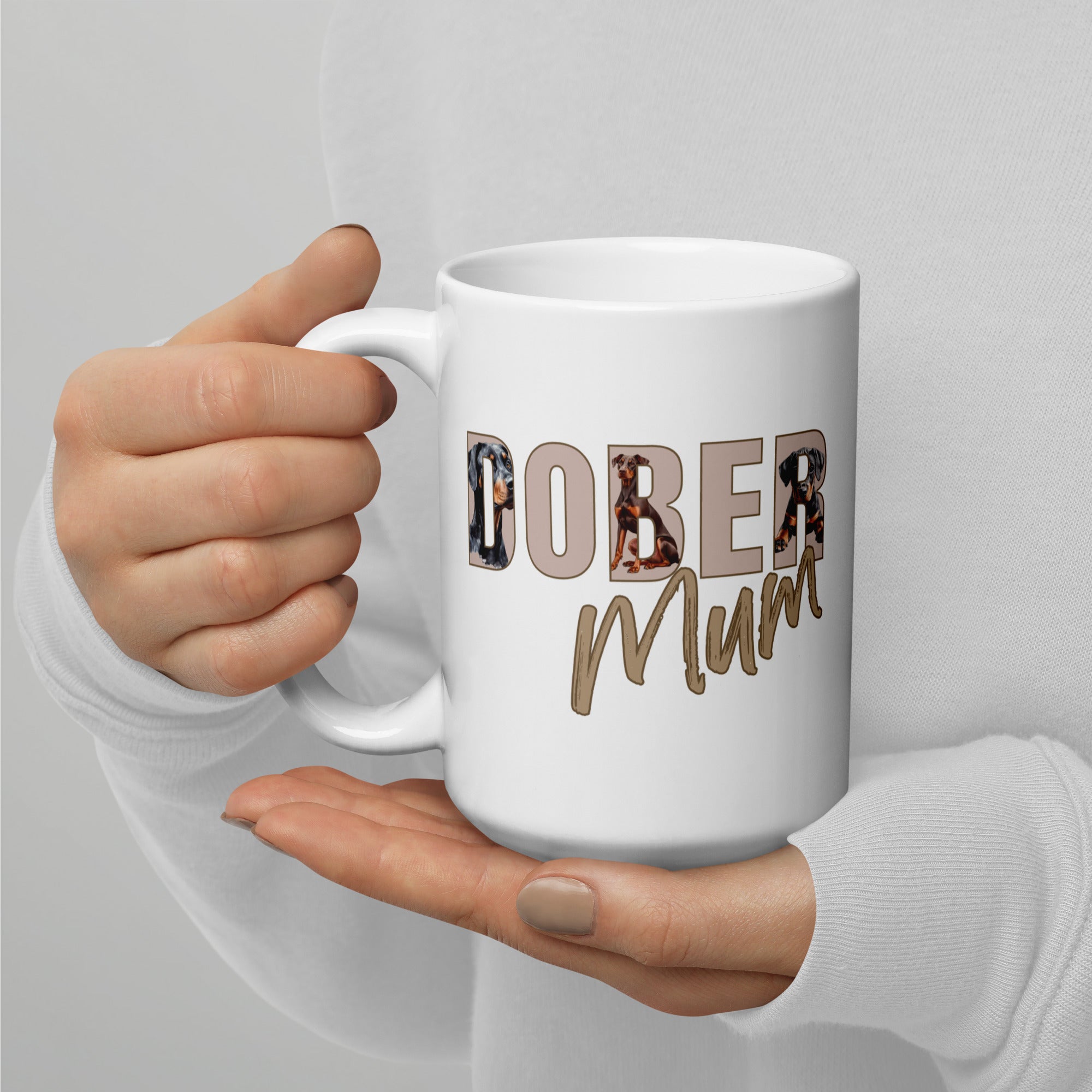 White mug with 'DOBER Mum' text held by a hand against a light gray background